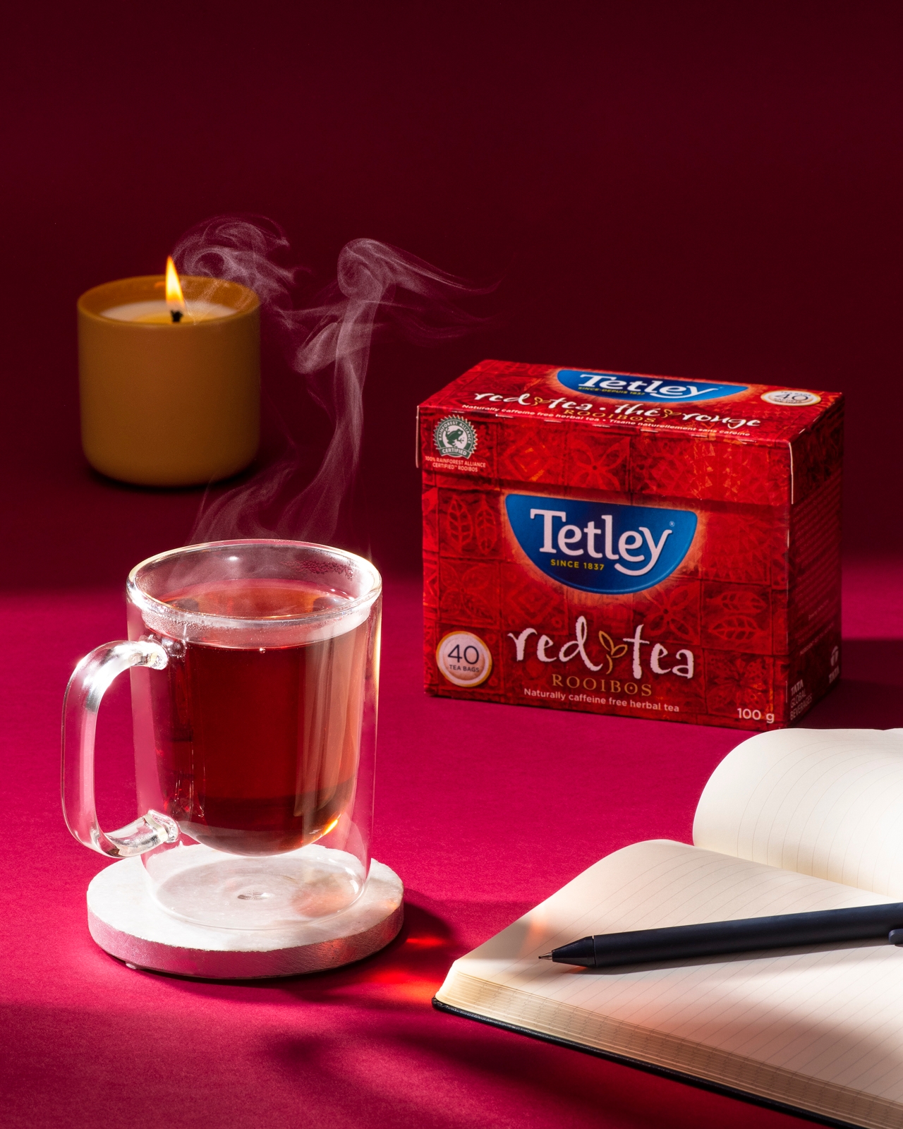 Box of Tetley Rooibos tea next to a clear mug with steeped tea. 