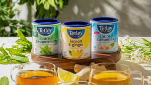 Tetley Pure Peppermint, Lemon & Ginger, and Pure Camomile tea canisters displayed on a wooden board and surrounded by fresh ingredient cues. 